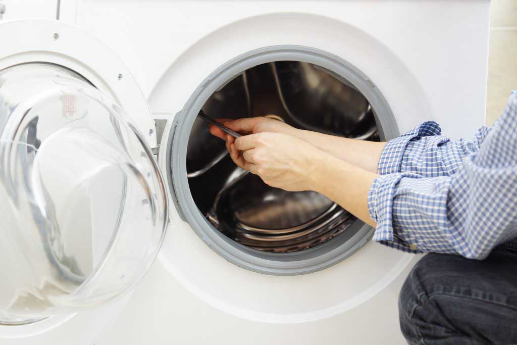 A repair man in a blue shirt working on a clothes washer