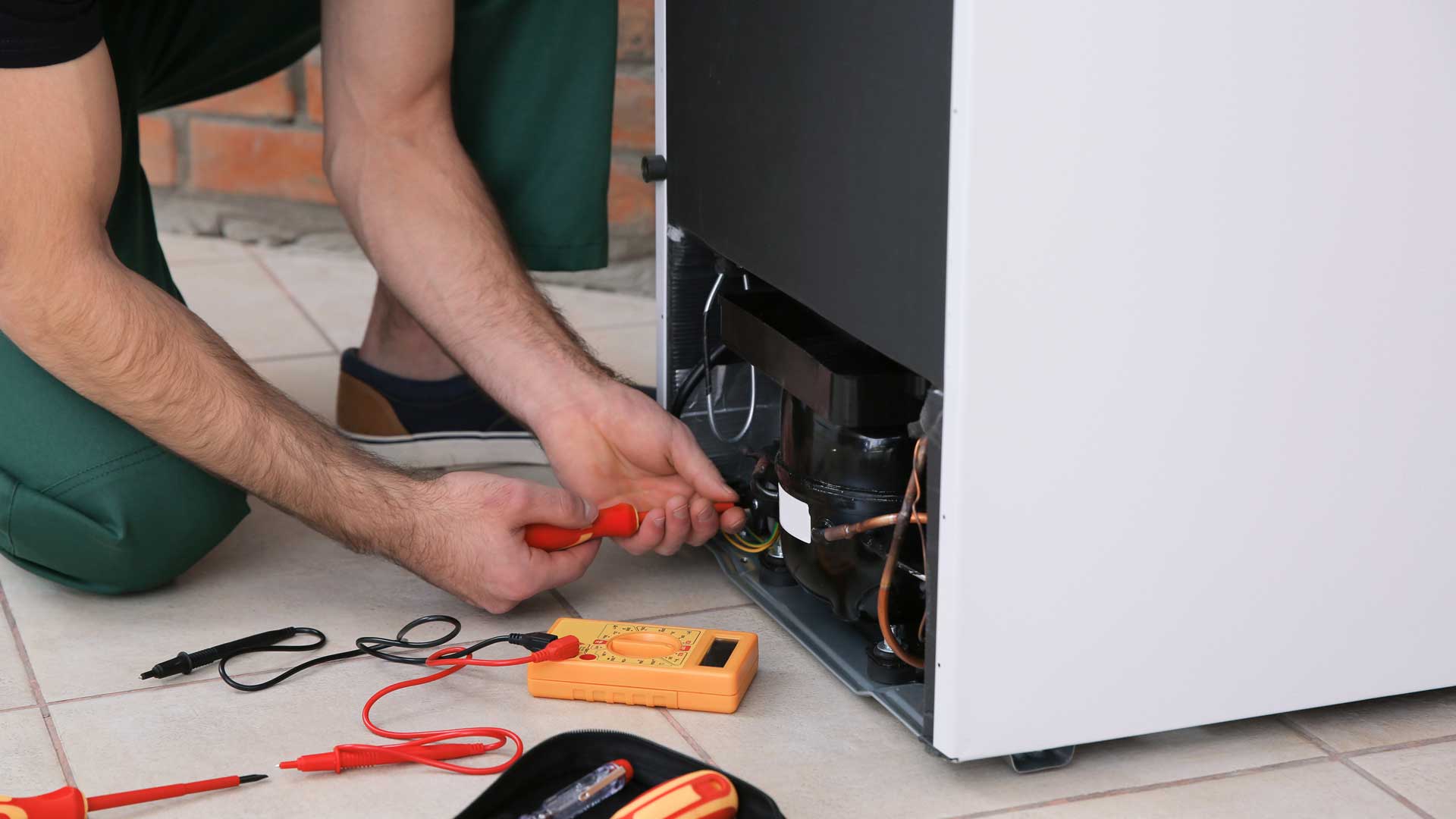 A man tinkering with exposed wiring at the back of a refrigerator